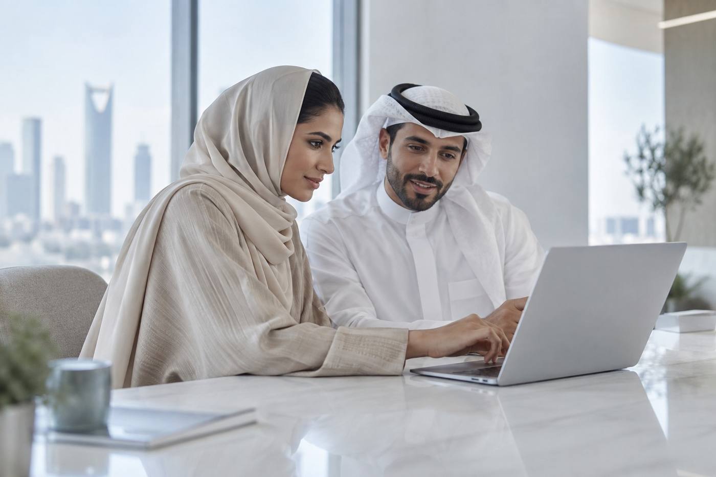 Two colleagues working through a screen together at a laptop in a bright Riyadh office.